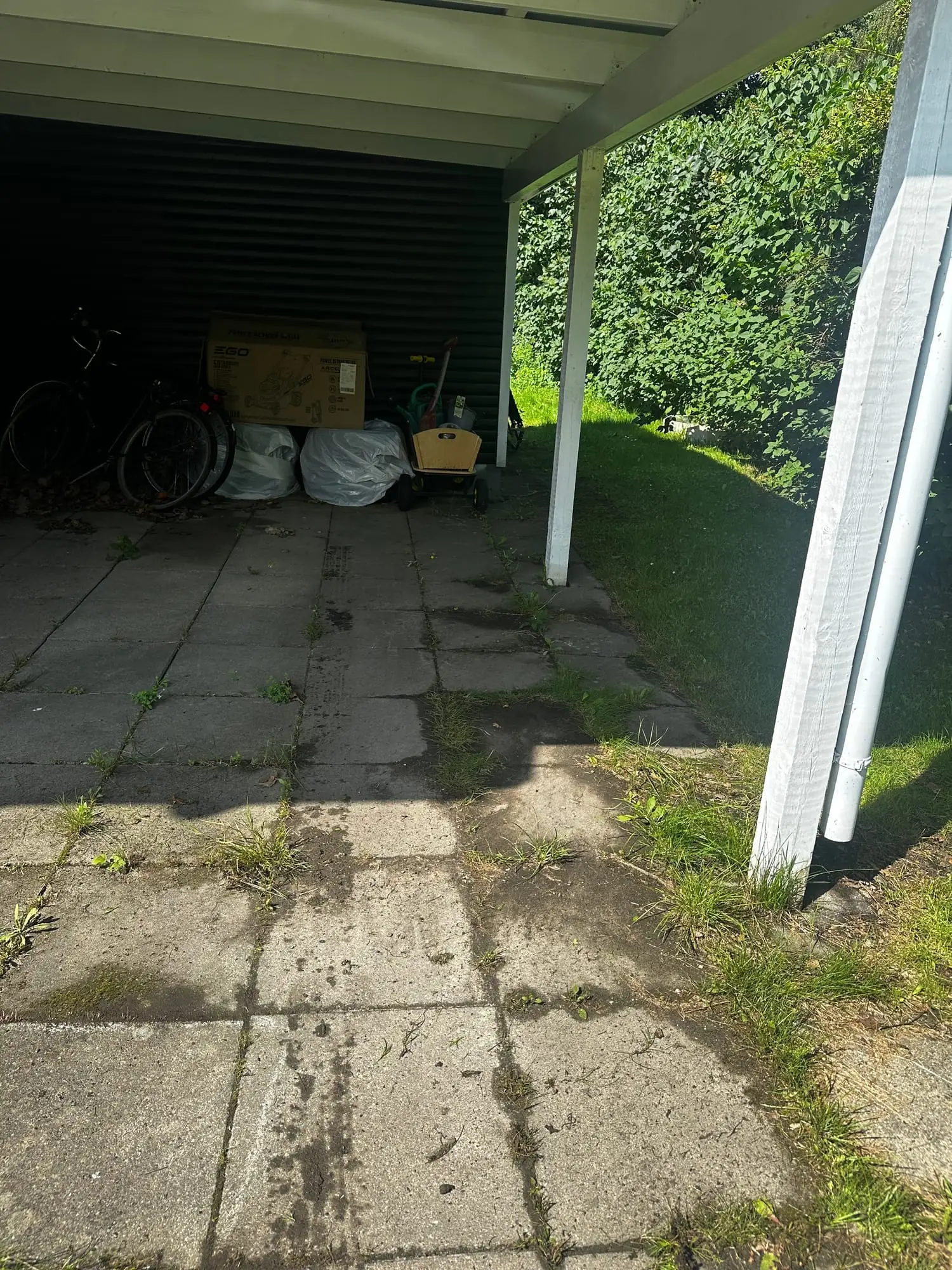 Flisebelægning under carport med ukrudt og mos i fugerne